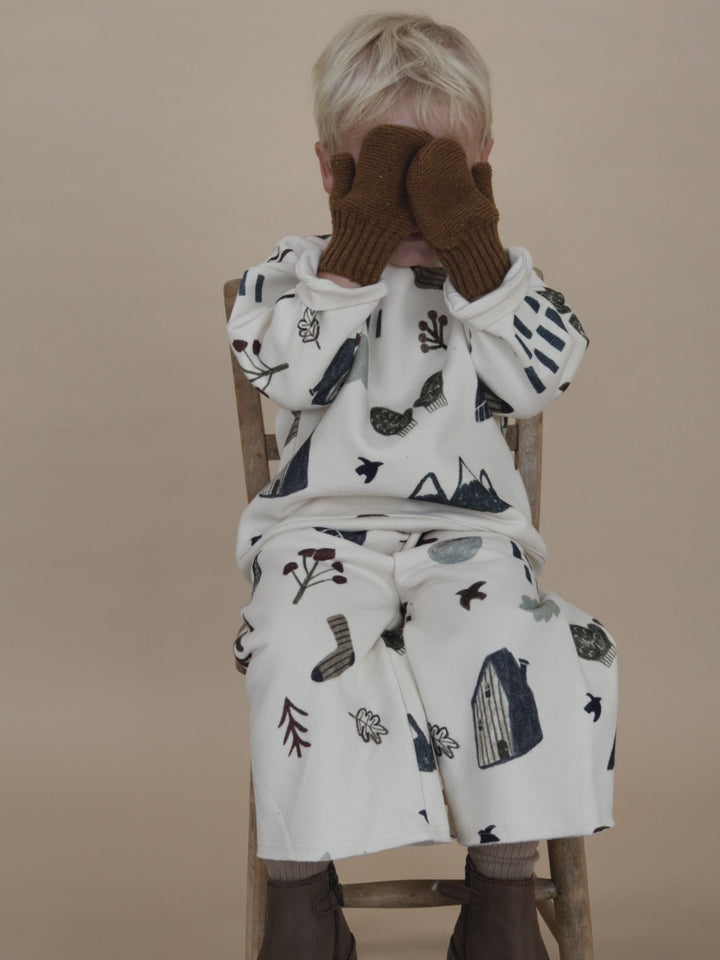 toddler wearing matching sweatshirt and pants set with brown wool mittens, playing peekaboo