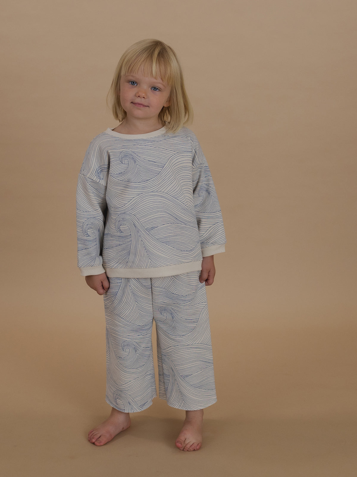 toddler in cream cotton sweatshirt with blue Seascape line-drawn ocean waves and matching pants