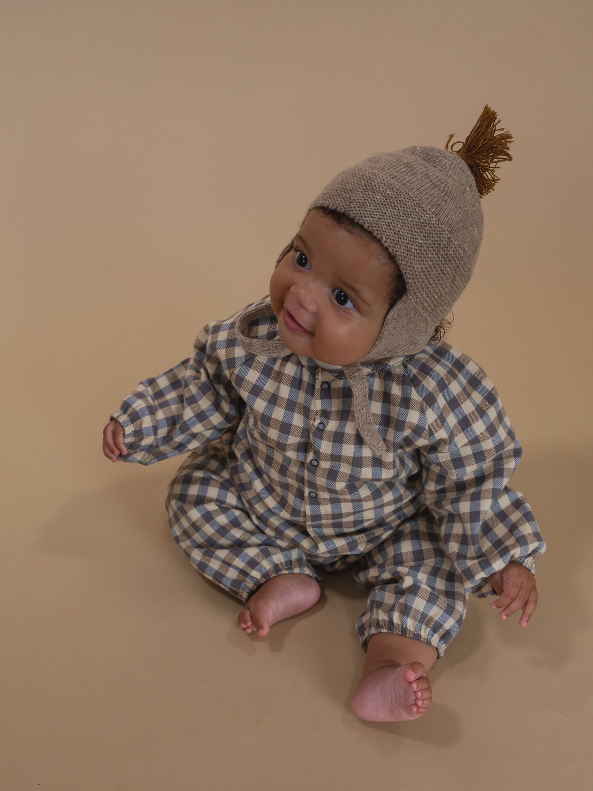 baby in cream and blue gingham flannel onesie with gathered cuffs, and oatmeal wool tassel hat
