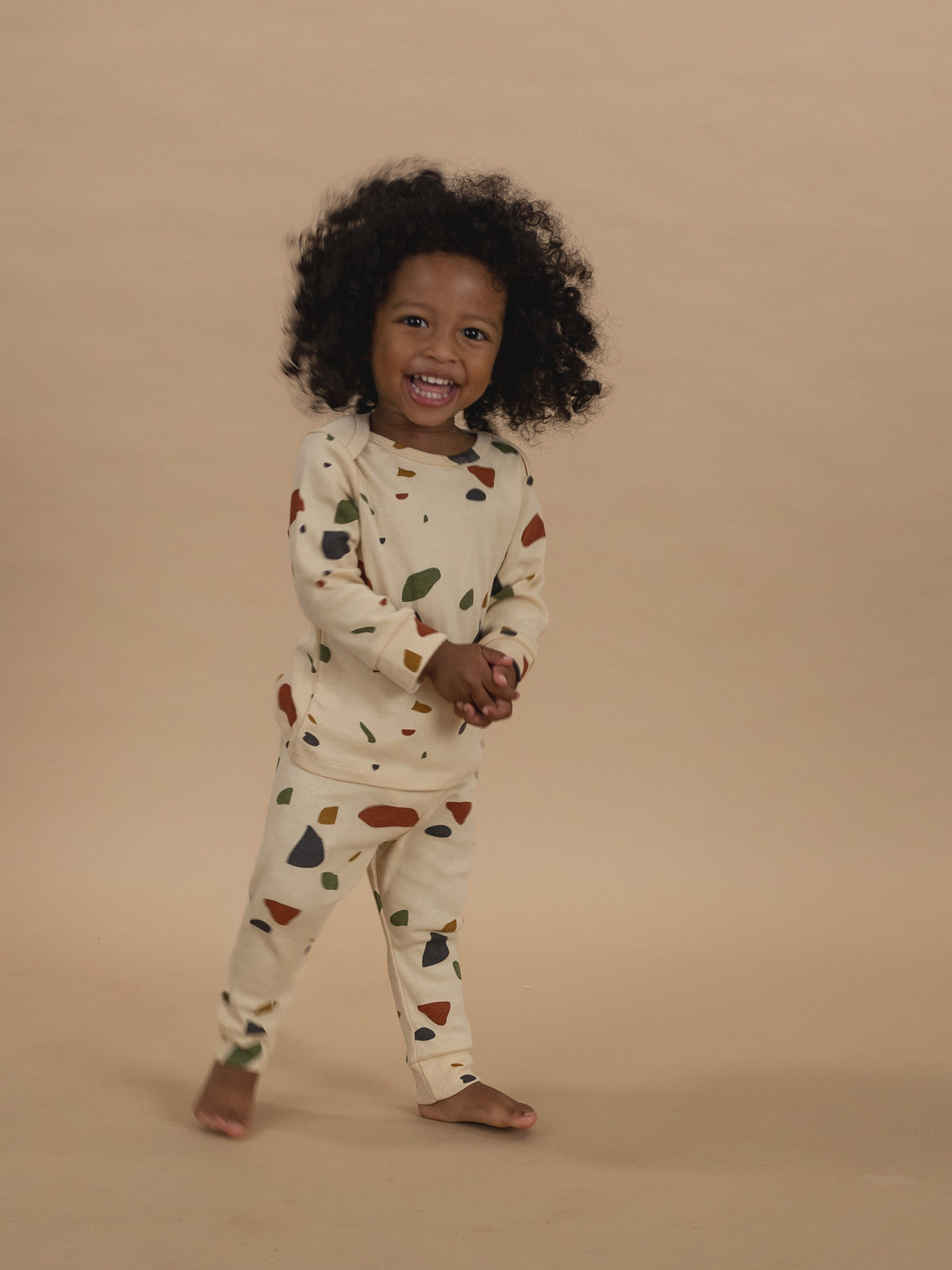 toddler in cream ribbed cotton long-sleeved top & leggings set with terrazzo print, smiling