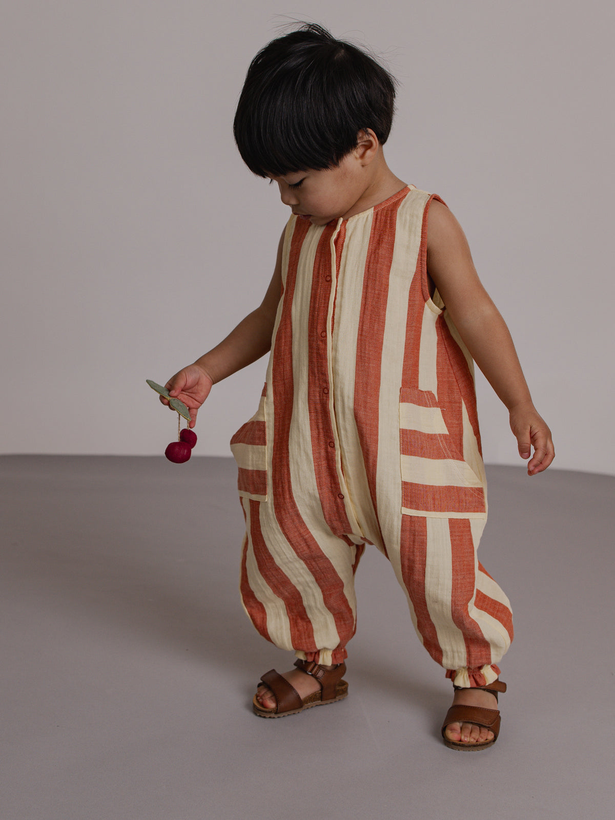 Child wearing a red and beige striped romper on a plain background
