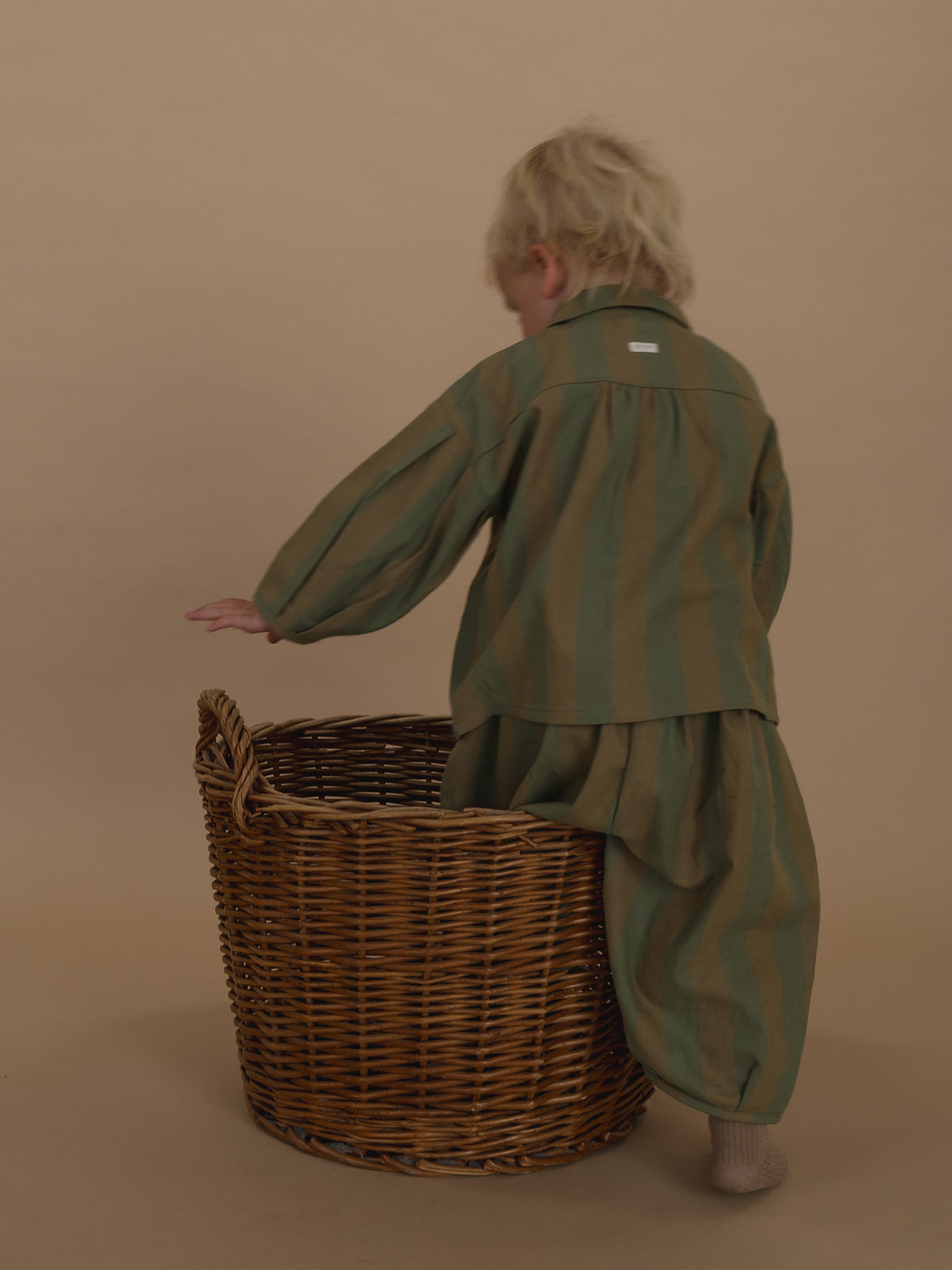 toddler wearing balloon pants in cream and green stripes with matching lodge shirt, stepping into basket