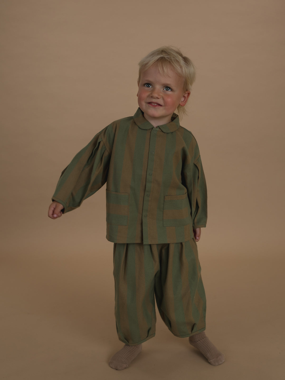 toddler wearing balloon pants in cream and green stripes with matching lodge shirt, swinging arms