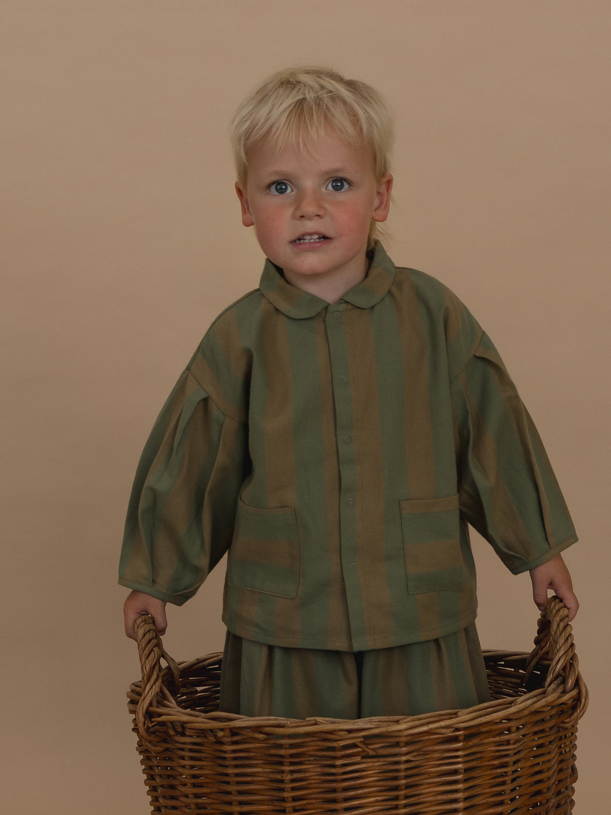 toddler in stripes lodge shirt with round collar & balloon sleeves & matching trousers standing in basket